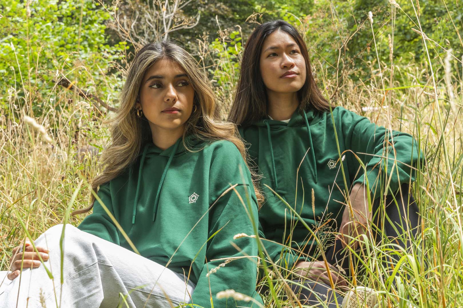 Two people wearing green hoodies sitting in a grassy field.